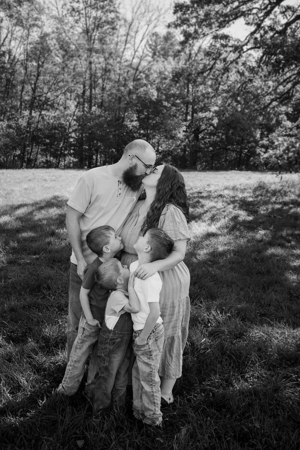 Black and white photo series showing a family embracing outdoors in a natural setting with trees in the background.