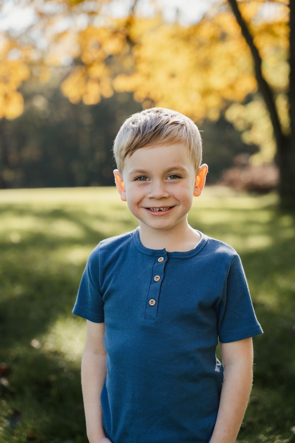 A sequence of four outdoor portraits showing a child in a blue henley shirt against a sunny autumn background.