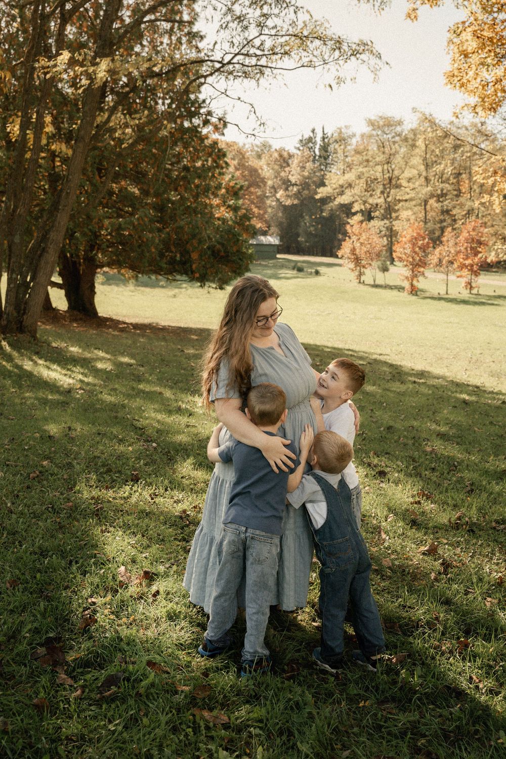 Family shares tender moments together on a grassy hillside during golden autumn afternoon light.