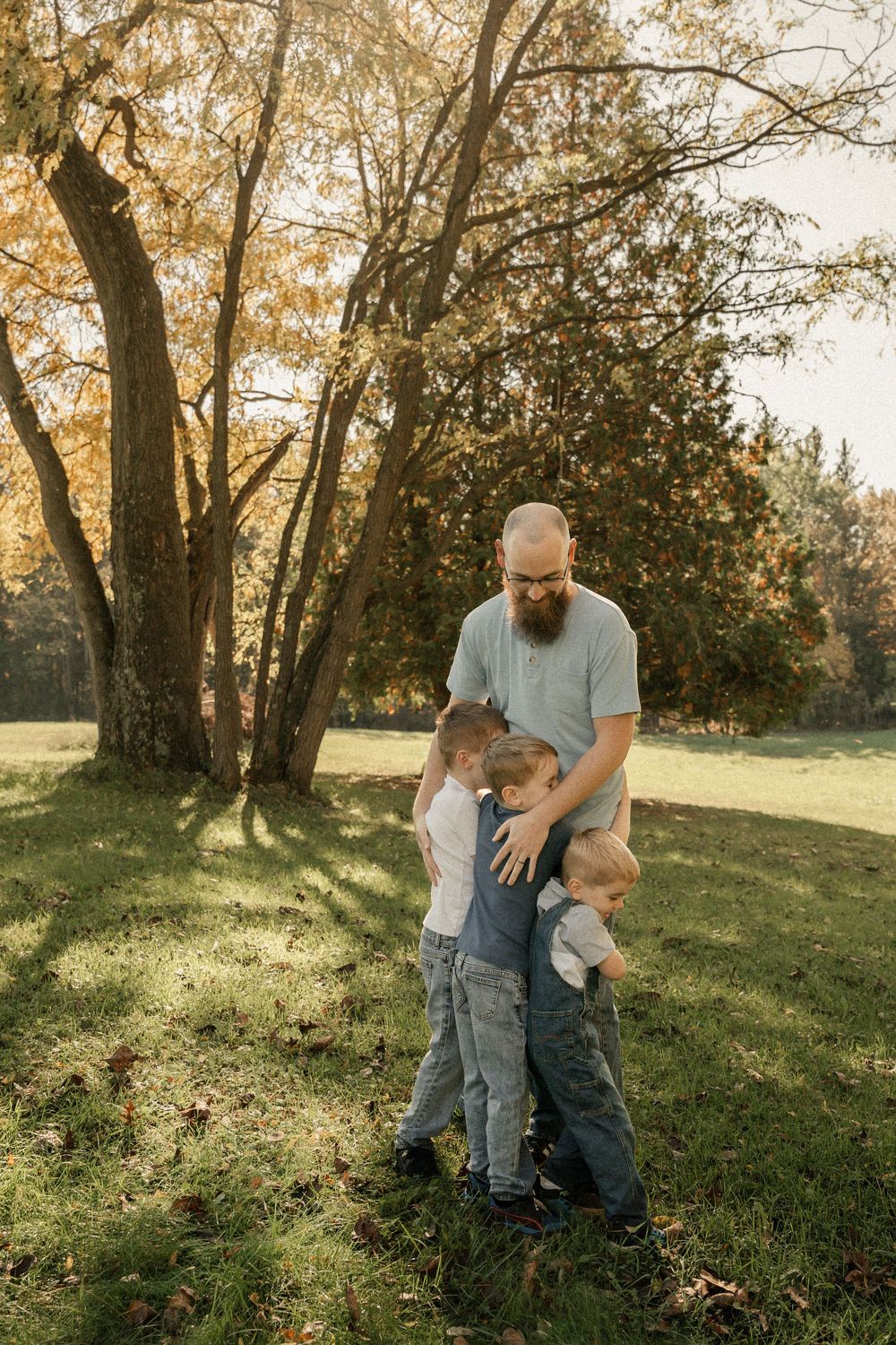 A playful outdoor scene with fall foliage showing adults and children interacting on a grassy hillside.
