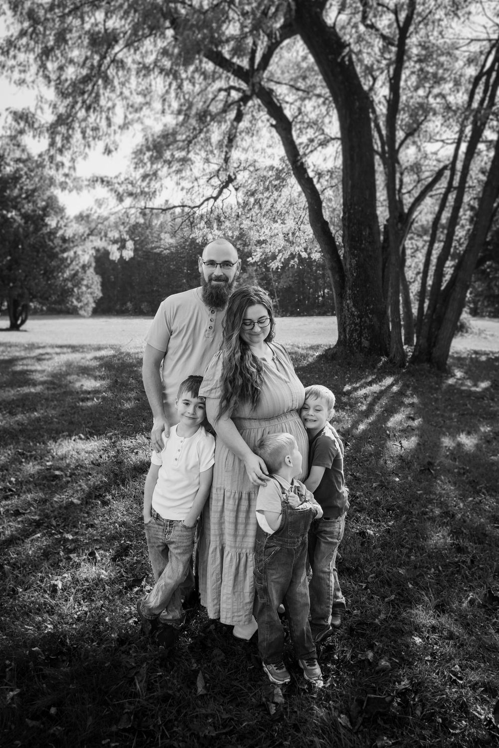 A black and white portrait of a group standing together under large trees in a park setting.