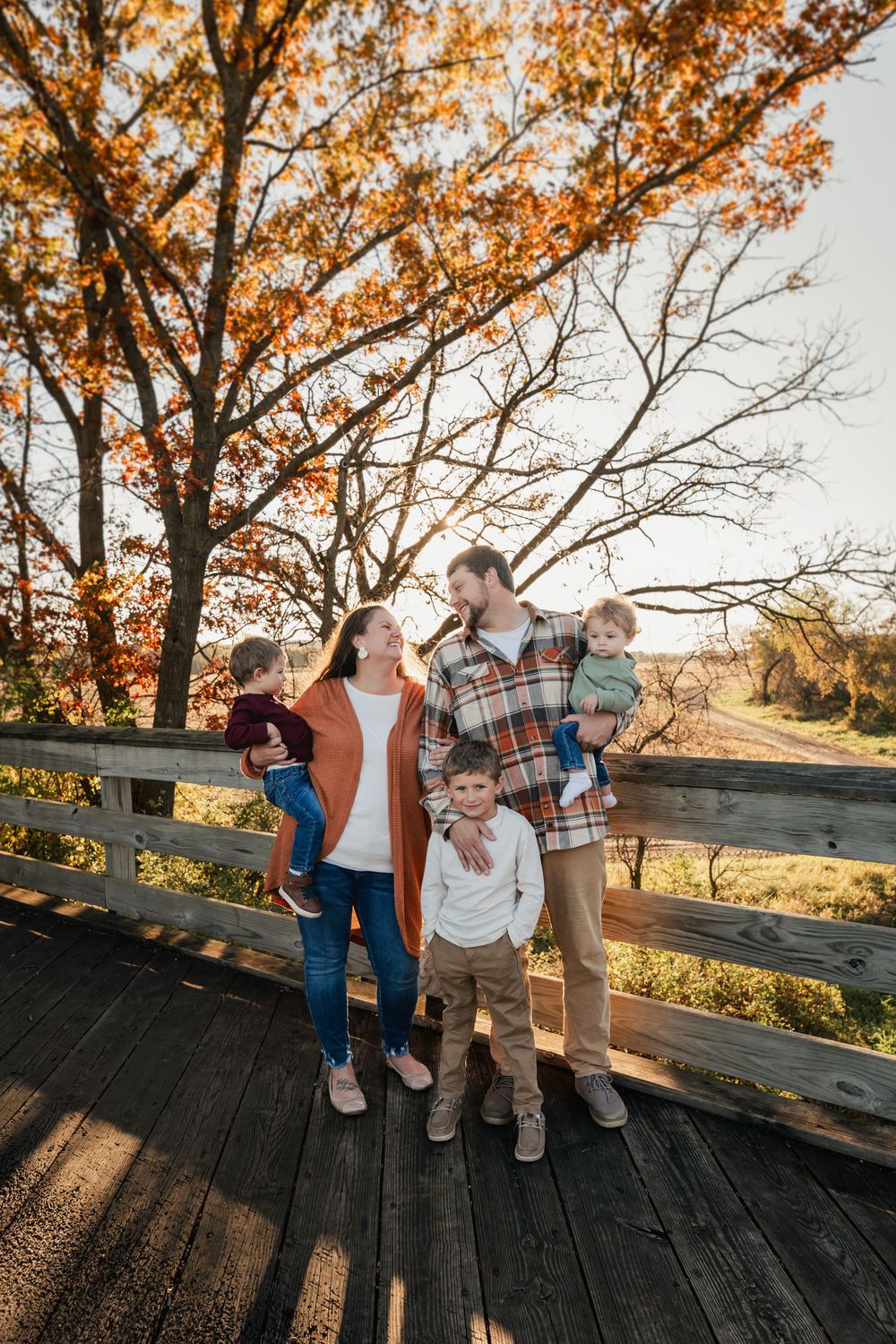 Family enjoying autumn sunset together on rustic wooden deck surrounded by golden fall foliage.