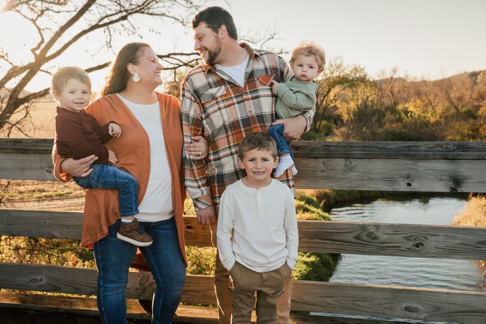 Family enjoying a warm sunset moment together by a rustic wooden fence in an outdoor natural setting.