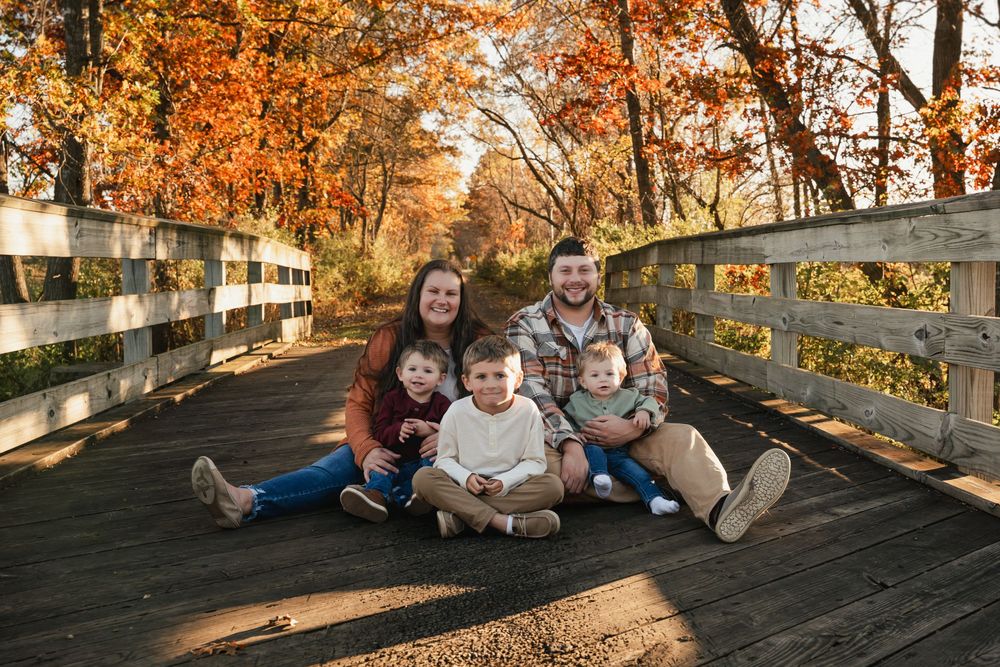 A group sits together on a wooden bridge surrounded by vibrant autumn foliage during golden hour.