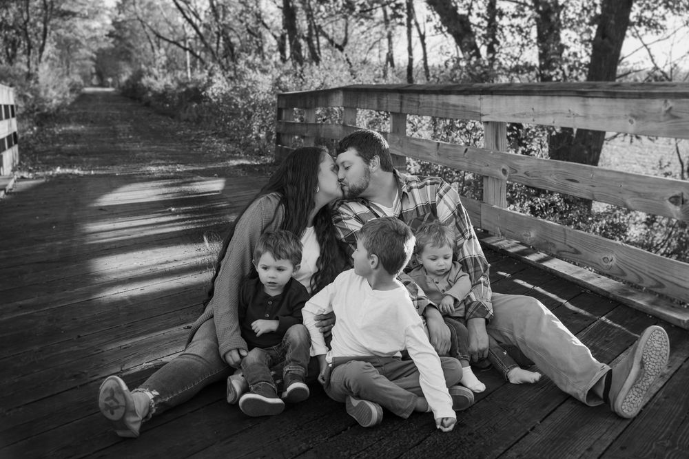 A family sits together on a wooden park bench in black and white, sharing a joyful moment outdoors.