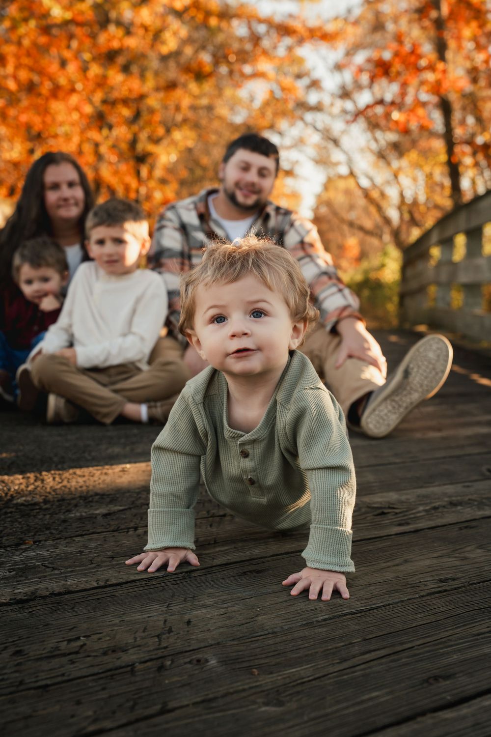 A child crawls on a wooden deck surrounded by vibrant autumn foliage with orange leaves in the background.