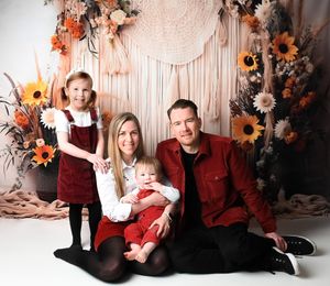 Family photo session with burgundy and black outfits against floral autumn backdrop.