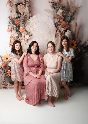 Women posing together in coordinated pink and silver dresses against a floral wall backdrop.