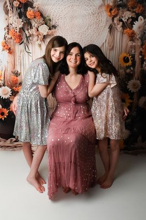 Group photo of friends in sparkly dresses against floral backdrop with orange and white decorations.