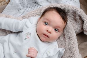 Close-up portrait of newborn baby wrapped in soft gray blanket.