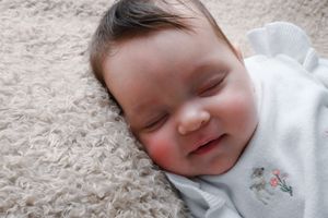 Sleeping baby wearing white outfit on soft gray blanket.