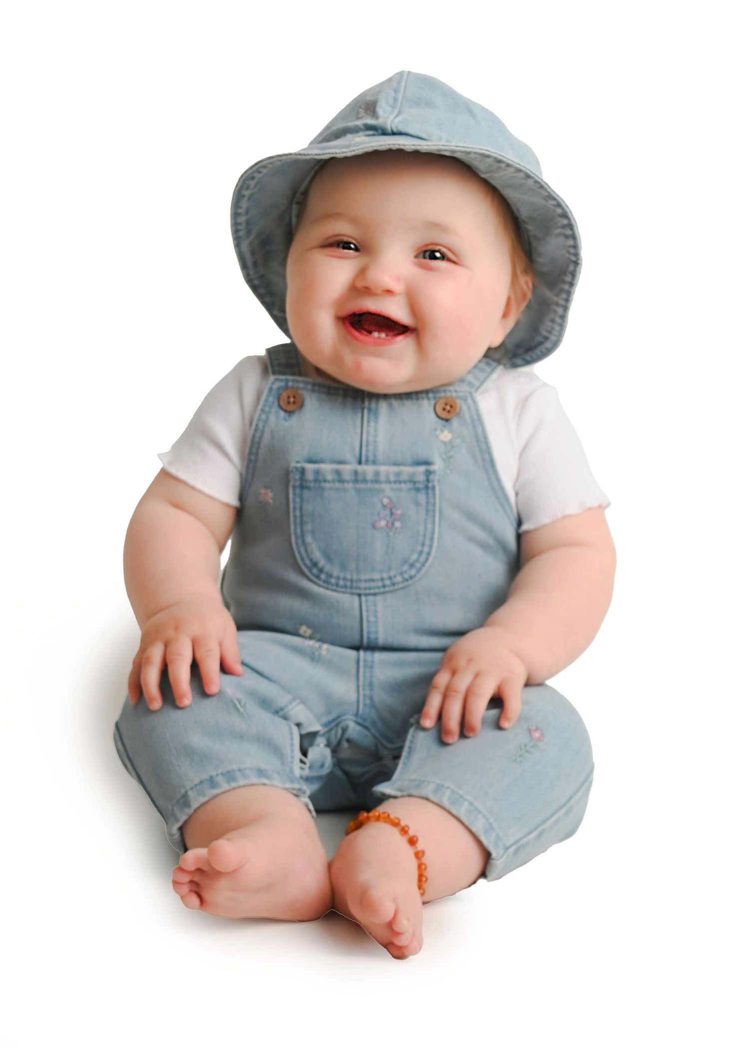 Baby wearing light blue overalls and hat photographed against white background.