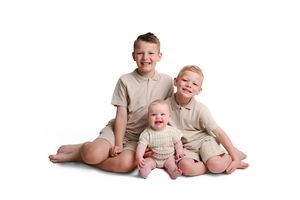 Siblings sitting together on white background in casual outfits.