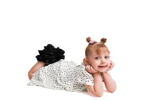 Baby in polka dot dress lying on white furry rug.