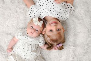 Baby wearing spotted white dress laying on plush white carpet.
