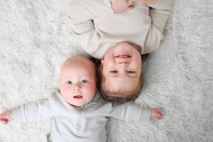 Family lying on white fluffy rug wearing cream colored outfits.