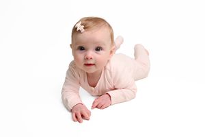 Baby in pink outfit crawling and smiling on white background in series of poses.