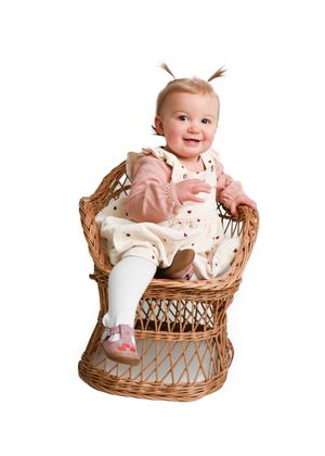 Smiling baby sitting in woven wicker basket wearing floral outfit.