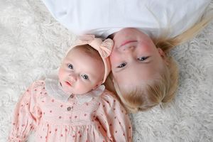 Baby lying on fluffy white blanket wearing pink floral outfit.