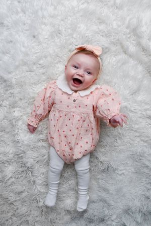 Baby in pink floral top and white leggings lying on plush white carpet.