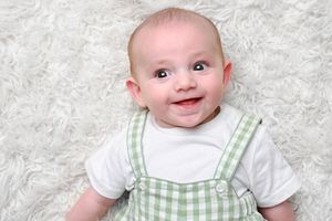 Baby wearing green gingham outfit smiling on white background.