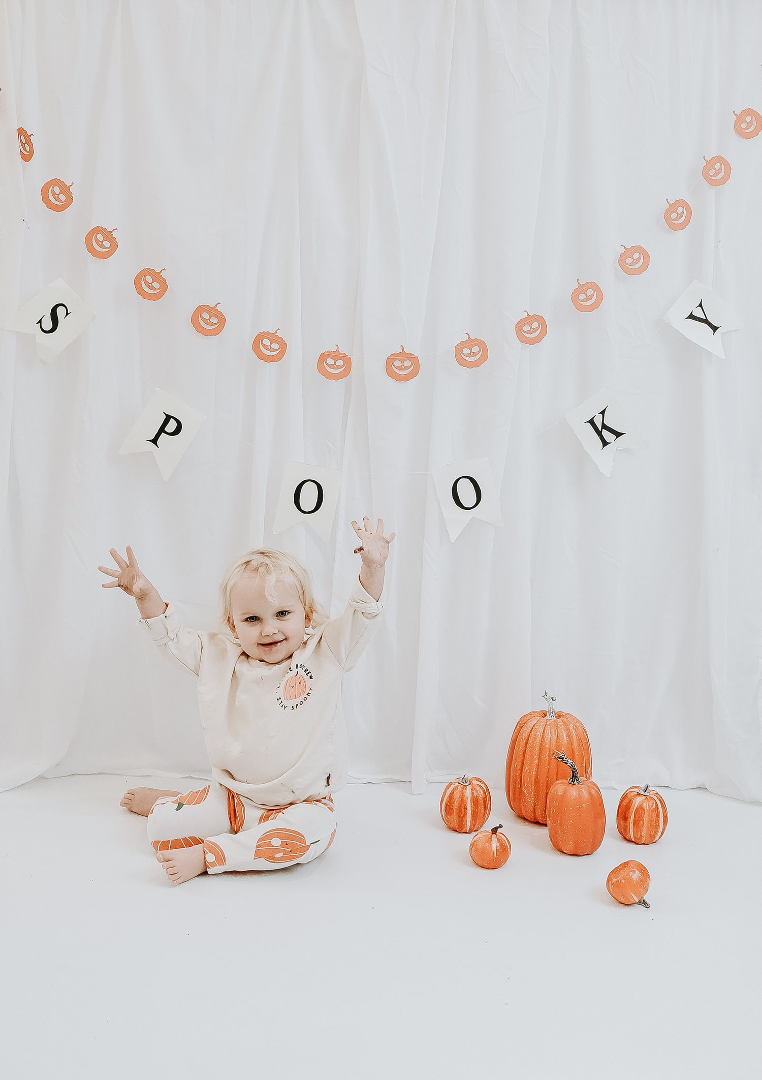 Minimalist photo setup with pumpkins and string lights against white backdrop.