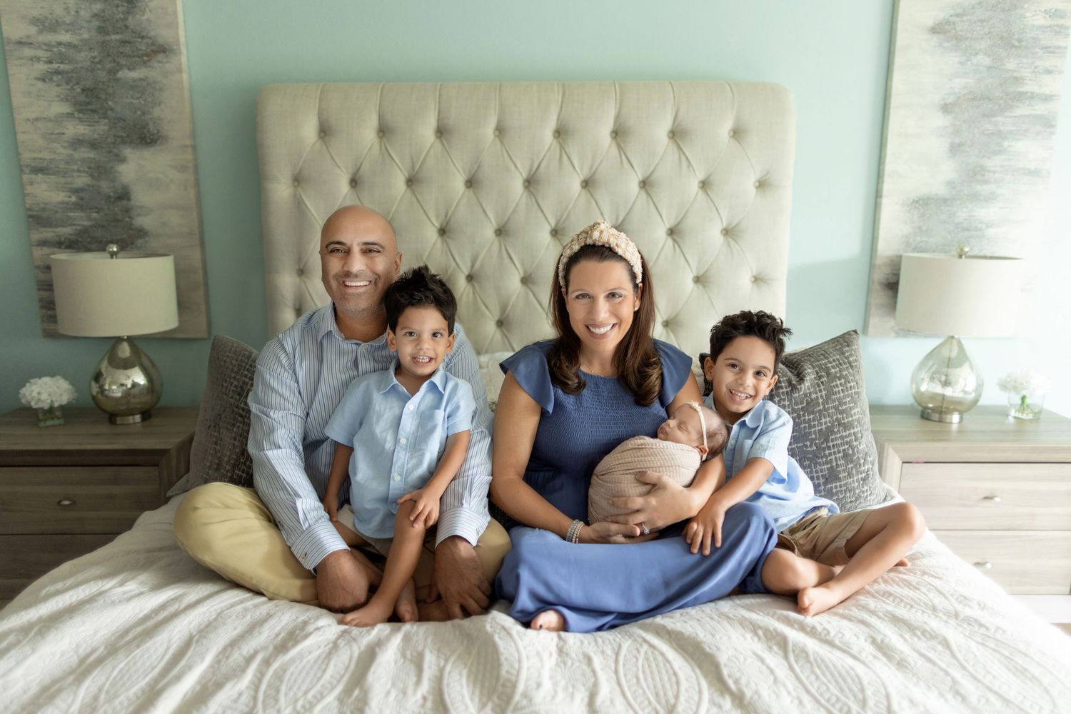 A family of five sits together on a bed, smiling and embracing in a cozy bedroom setting. Photos by Tampa Photographer DigitalMyst Photo