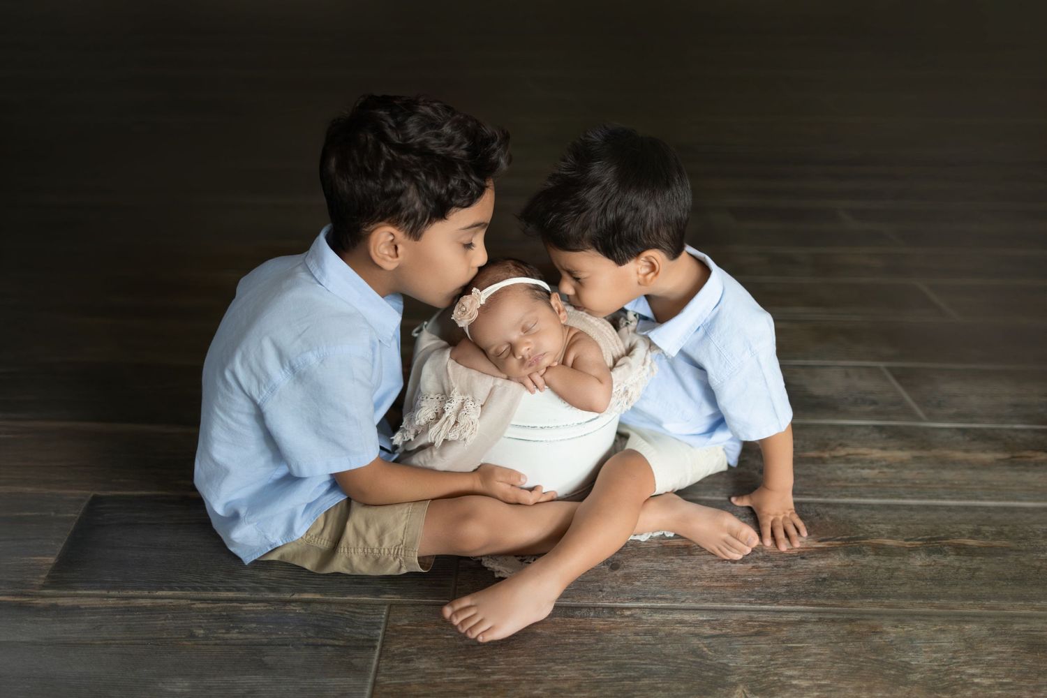 Three young children sitting on a wooden floor, gently interacting with a sleeping newborn baby. Photos by Tampa Photographer DigitalMyst Ph