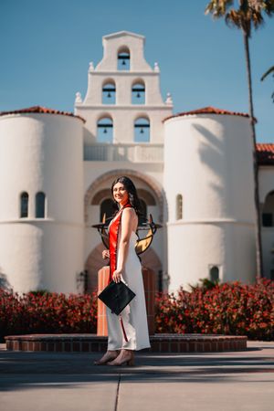 Graduate poses in front of Spanish colonial style building with white arches.