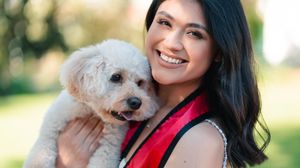 Graduate in red stole cuddles with small white fluffy dog outdoors.