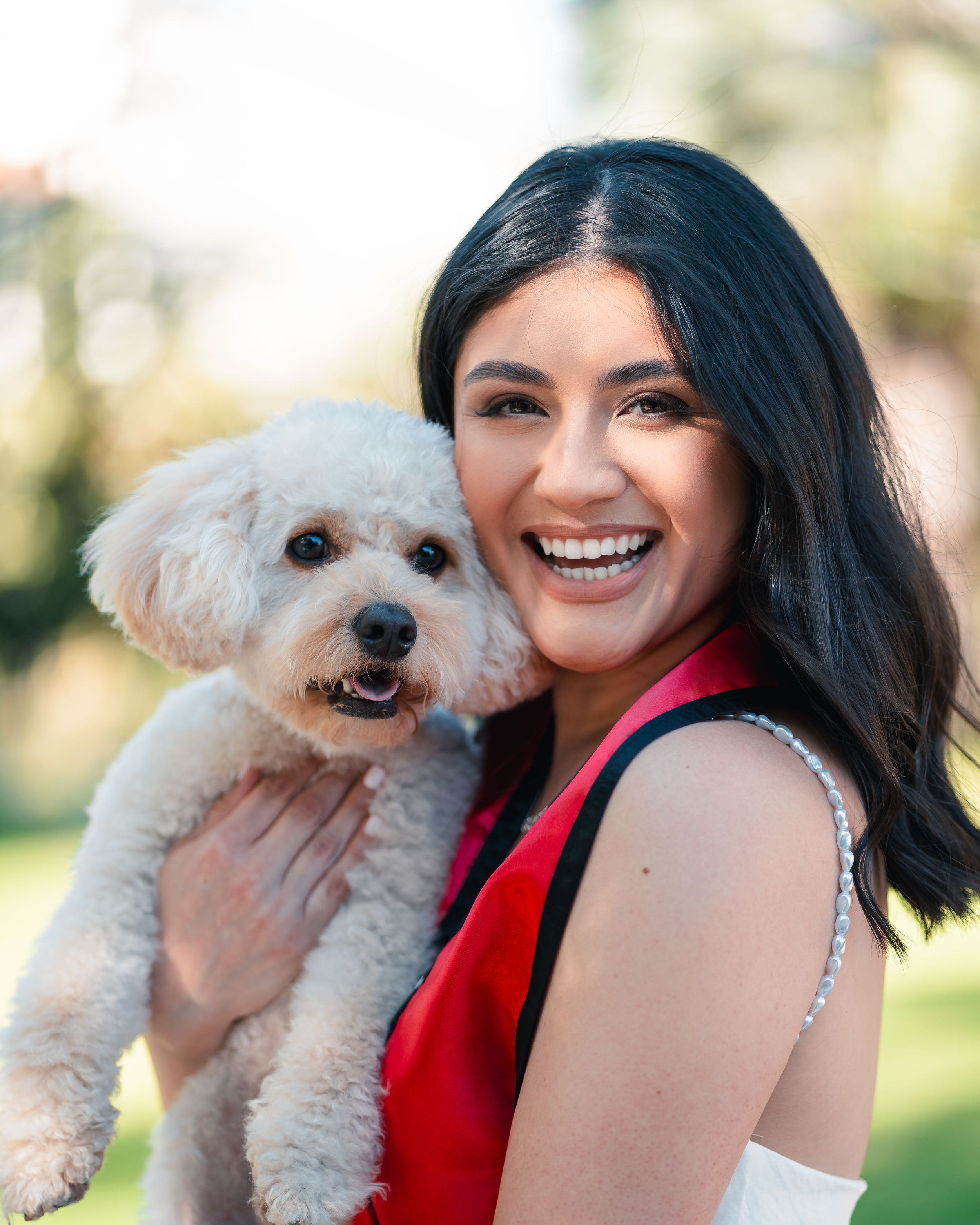 Graduate holding small white dog while wearing red graduation stole.