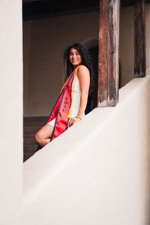 Graduate in red stole poses by architectural window frames.