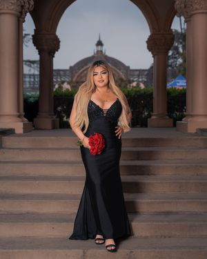 Elegant black gown portrait with red roses under ornate architectural arch.