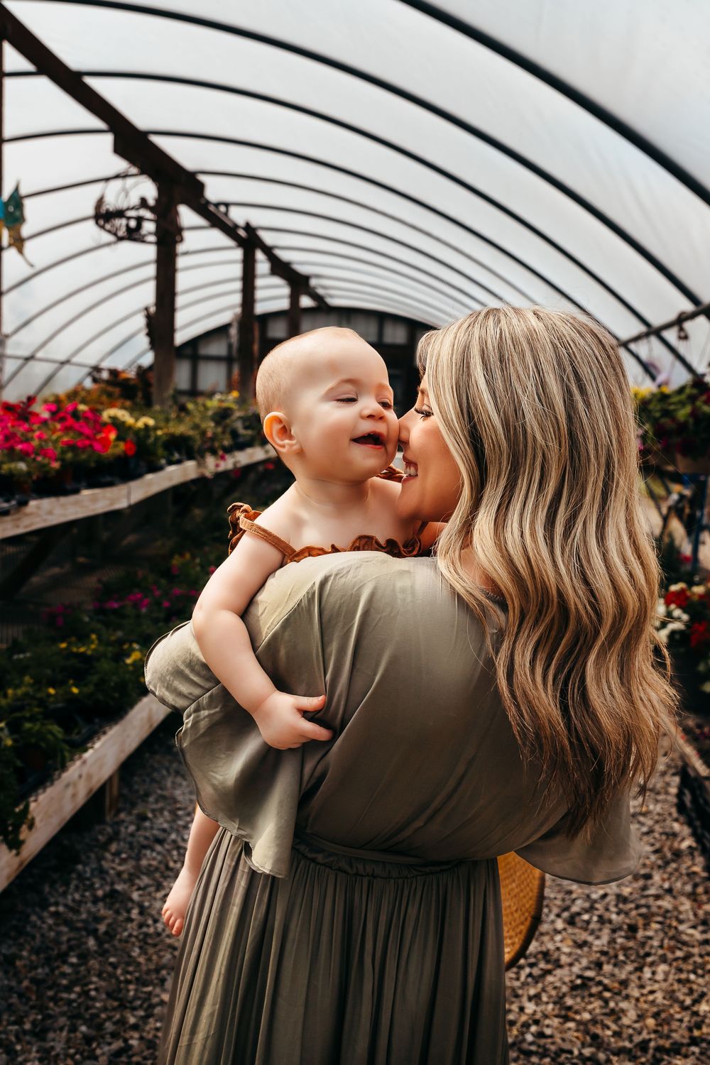 Sweet interaction between parent and baby in a greenhouse among red flowers.