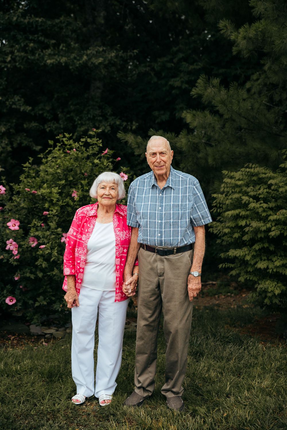 Outdoor portrait of a couple standing together in a garden with pink roses.