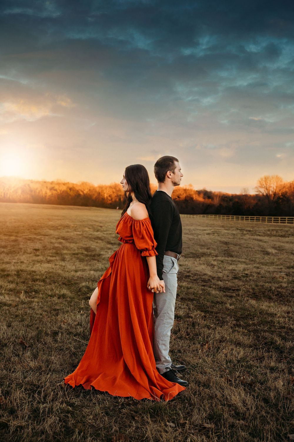 Sunset engagement photos in an open field featuring a dramatic red flowing dress.