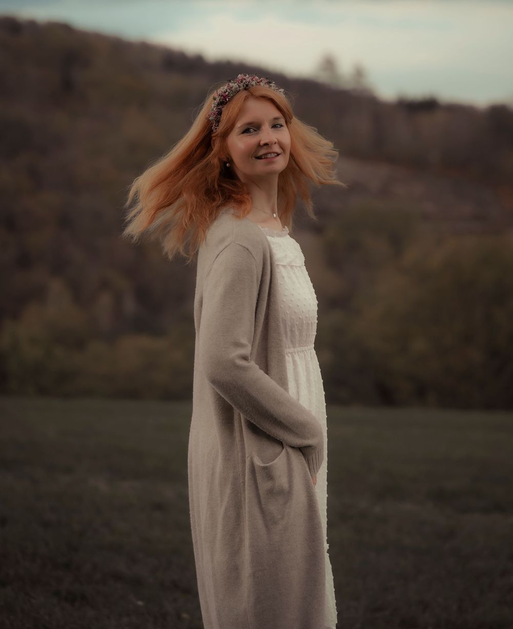 Eine Person in einem fließenden beigefarbenen Kleid dreht sich freudig auf einer Wiese in der Abenddämmerung.