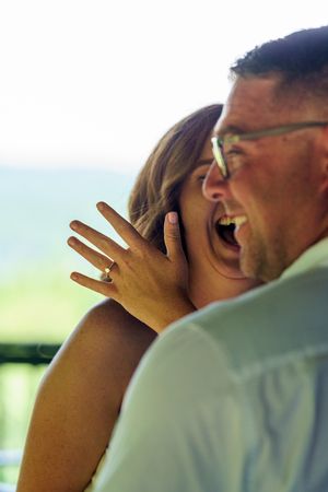 Laughing couple shares an intimate moment outdoors with engagement ring visible.