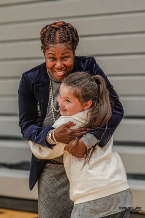 A heartwarming candid moment captures a joyful embrace between a coach and young student in a gym.