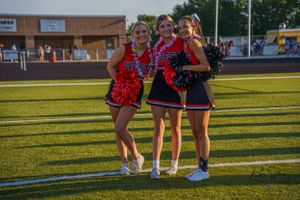 Three cheerleaders in matching uniforms pose together on football field at sunset.