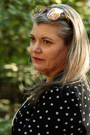 Woman in polka dot blouse poses outdoors with sunglasses on head.