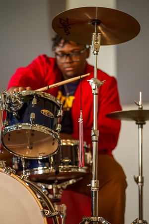 A drummer in a bright red sweater performs behind a professional drum kit during a musical performance.