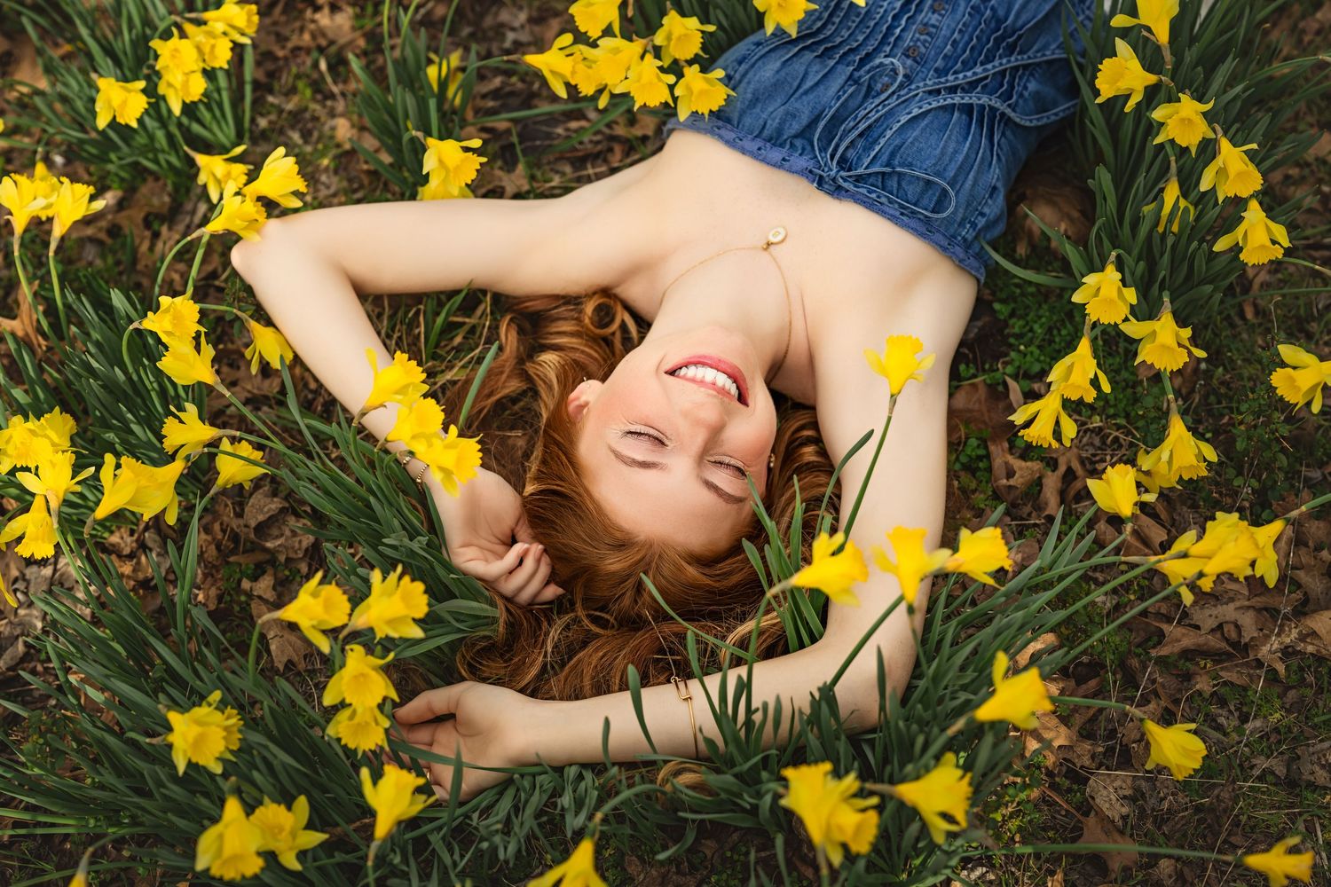 Senior girl with red hair lying down surrounded by blooming yellow daffodils for Spring Senior photo session in Chattanooga.