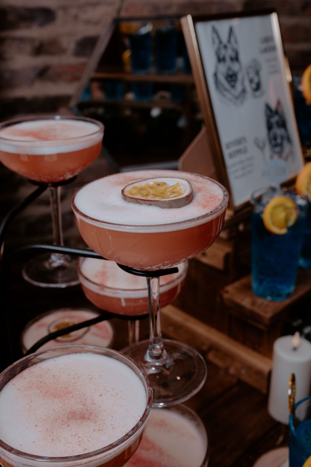 Elegant pink cocktails with frothy tops and passion fruit garnish displayed on a tiered stand at a bar.