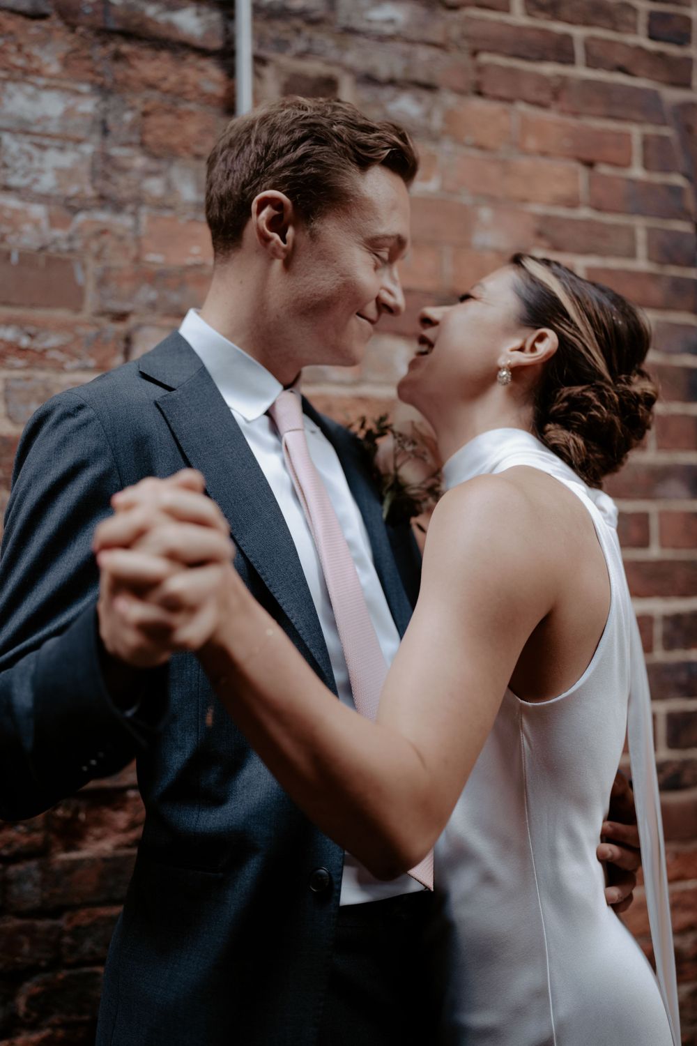 Elegant couple shares an intimate dance moment against a rustic brick wall.