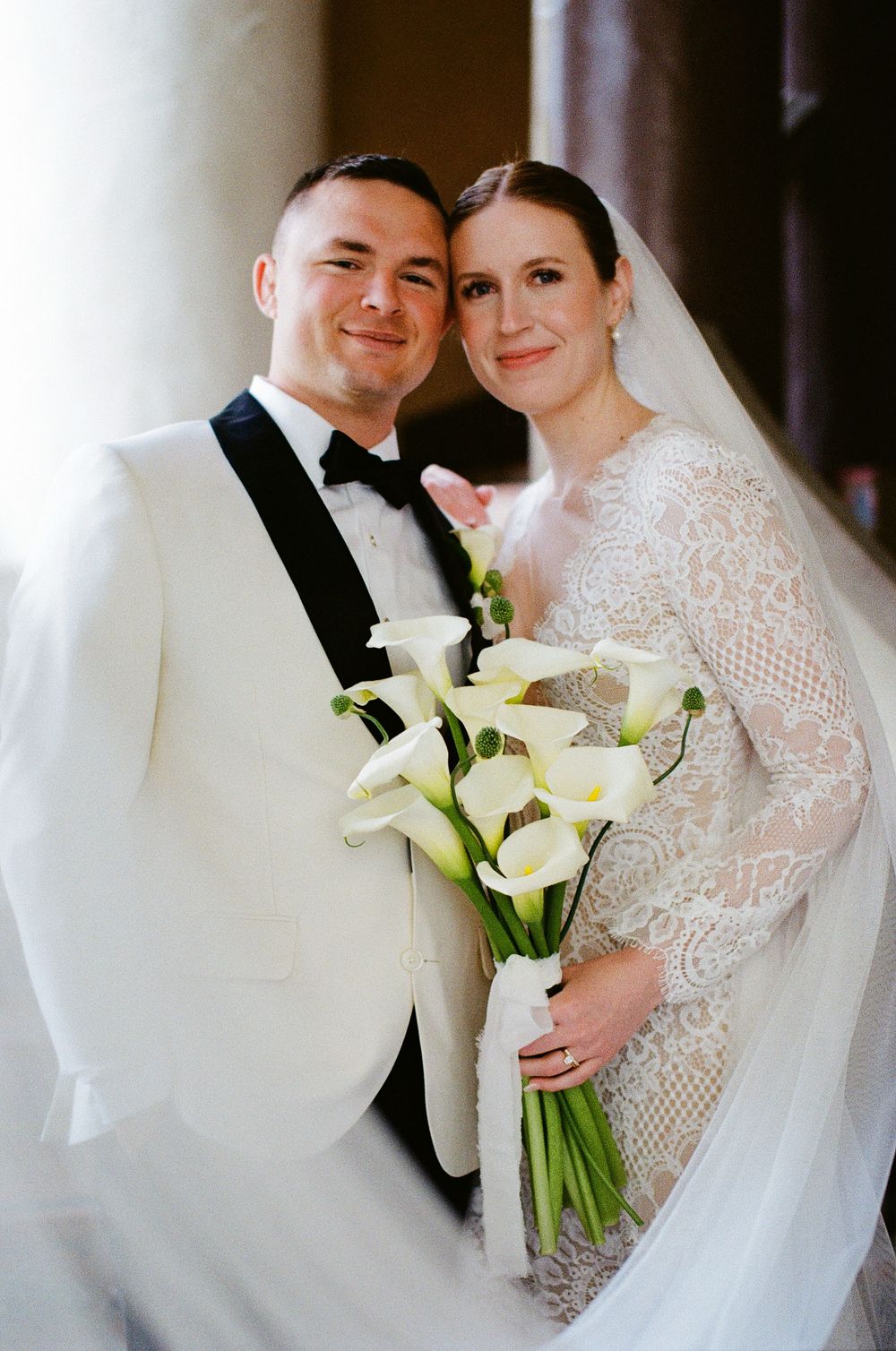 A classic film wedding photo of a bride and groom draped in a veil.