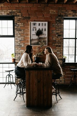 Two people having coffee at a wooden bar table in an industrial brick-walled cafe.