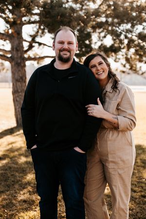 A casual couple posing outdoors during golden hour with pine trees in the background.