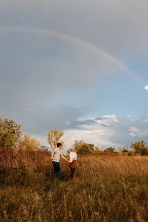 Beautiful rainbow arches across cloudy sky over golden field at sunset.