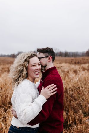 Couple embracing and laughing in golden autumn field with dried grasses.